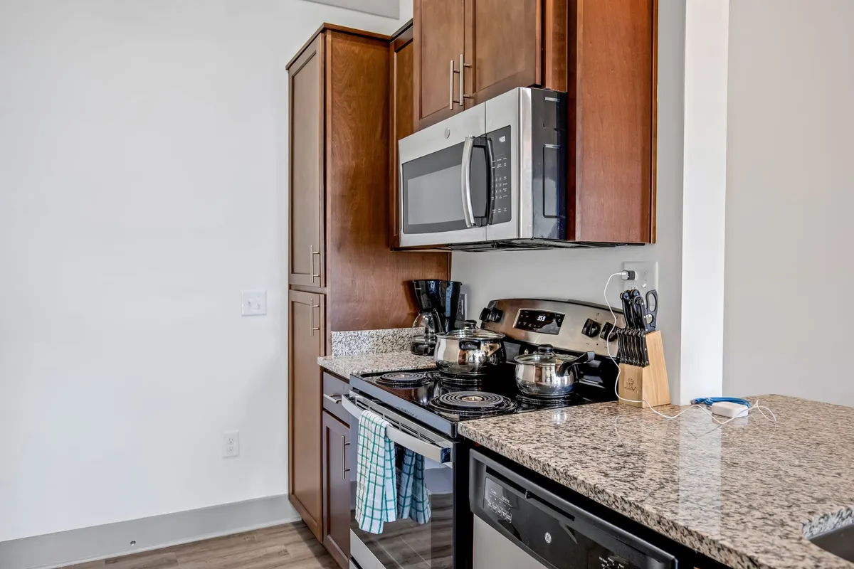 A welcoming, contemporary kitchen featuring stainless steel appliances, sleek granite countertops, and rich dark wood cabinets. The space looks uncluttered yet ready for meal preparation or entertaining guests, with modern fixtures and plenty of workspace on the counters.