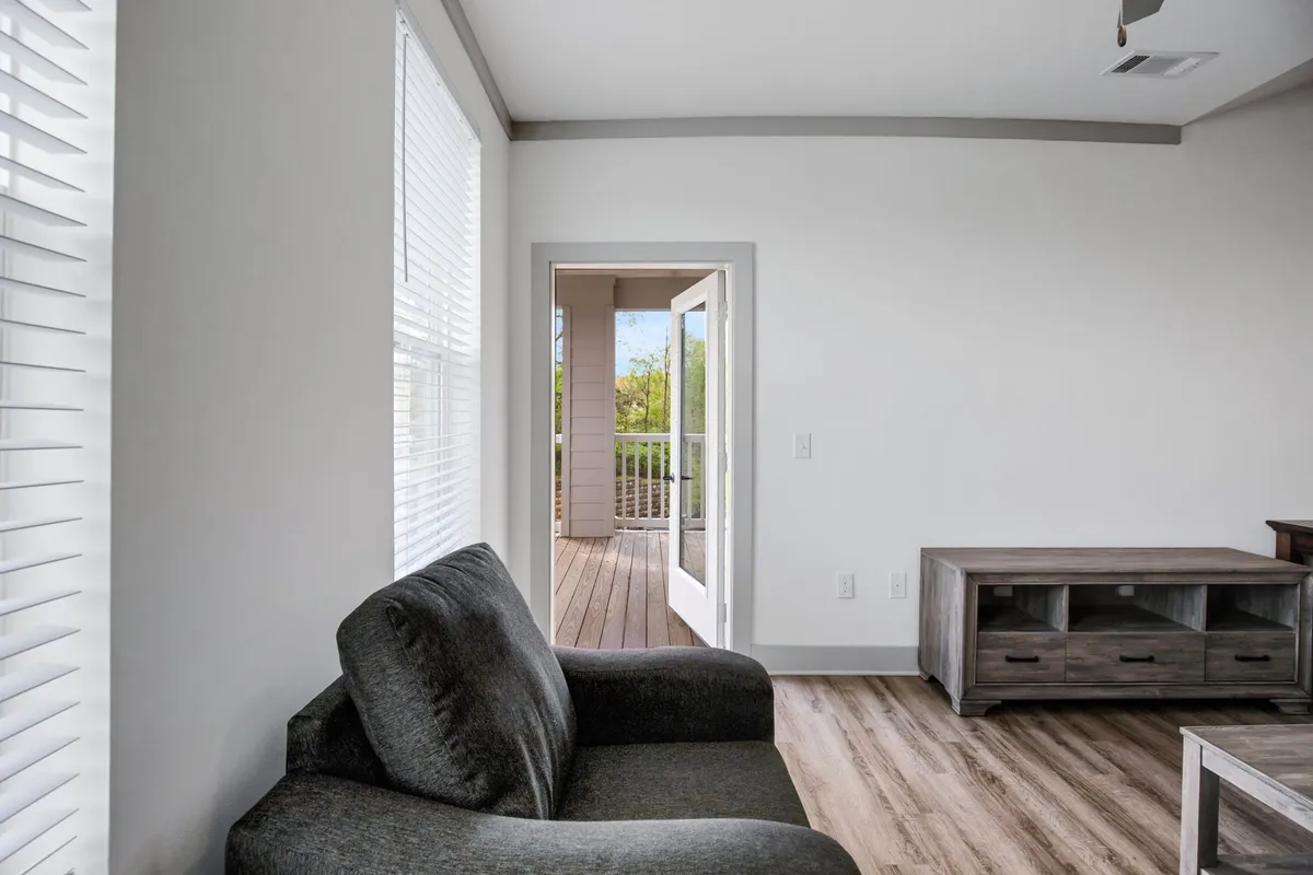 An inviting living space with a plush sofa, open doorway, sleek wooden floors, and a modern TV stand. Natural light streams in, enhancing the airy, welcoming vibe that makes the apartment feel instantly livable.