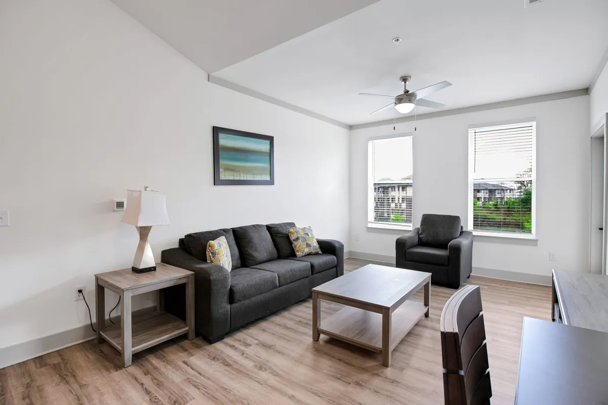 A bright, contemporary living room featuring a cozy sofa, a modern coffee table, striking wall art, and ample natural light pouring in from the windows. The space is accented by decorative lighting, creating a comfortable and stylish atmosphere ideal for relaxing or entertaining.
