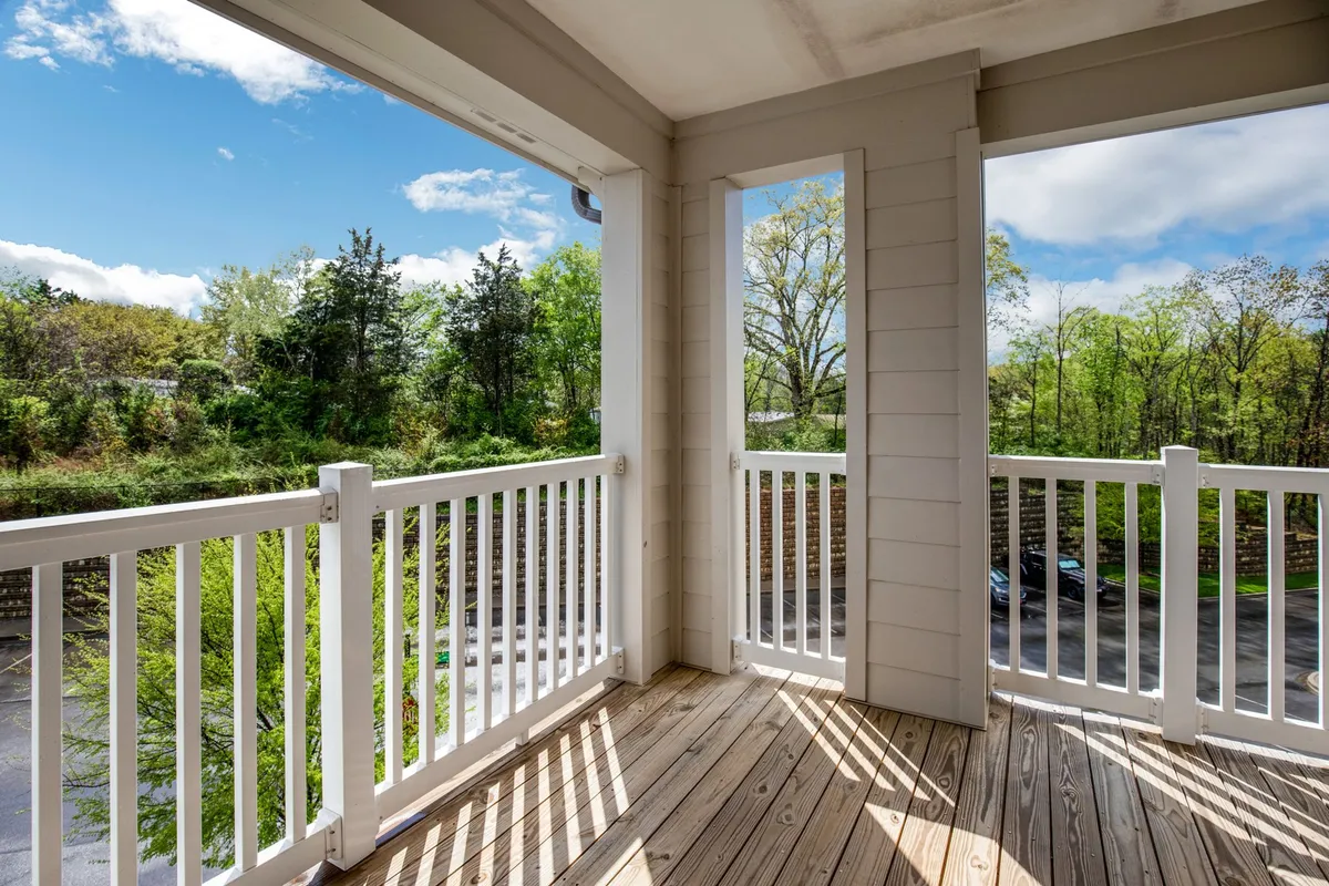 This image depicts a peaceful wooden deck with white railings surrounded by green trees and a blue sky. The setting invites relaxation, enjoying morning coffee, or quiet family moments in nature.