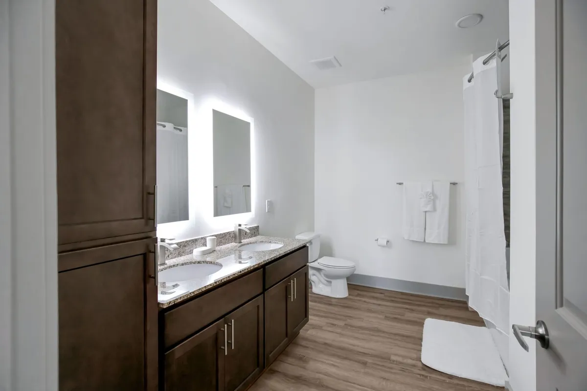 This bathroom features a double vanity with two sinks, expansive mirrors, and a tranquil, organized layout. The clean and modern design is perfect for individual routines and quiet moments of self-care.