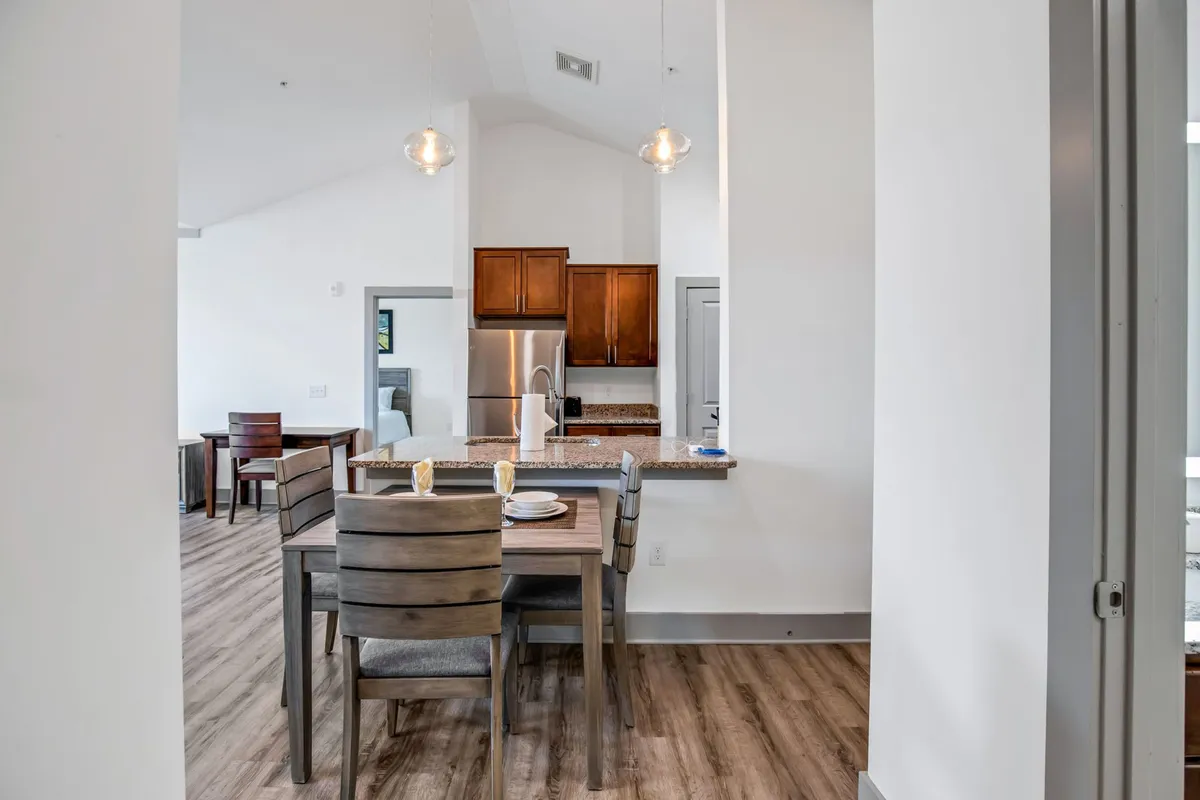 A modern dining area featuring a large dining table, sleek light fixtures, and a kitchen counter in the background. The setting is warm and inviting, ideal for shared meals and hosting lively discussions with friends or family.